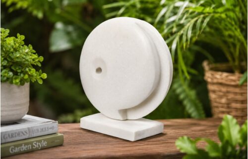 Modern white marble abstract sculpture displayed in a stylish garden setting with natural greenery and contemporary outdoor decor.