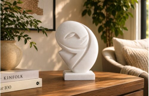 Modern white abstract sculpture displayed on a wooden table in a stylish living room with indoor plants.