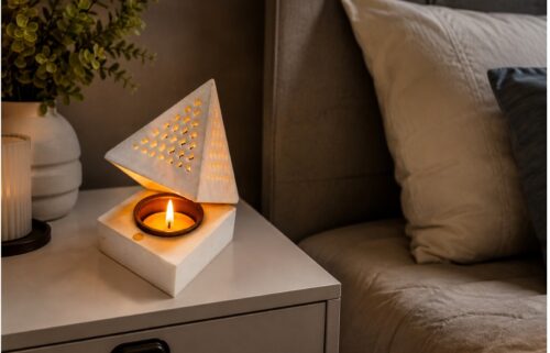 Modern white marble tealight candle holder with geometric pyramid design placed on a bedside table, creating a warm and luxurious bedroom ambiance.